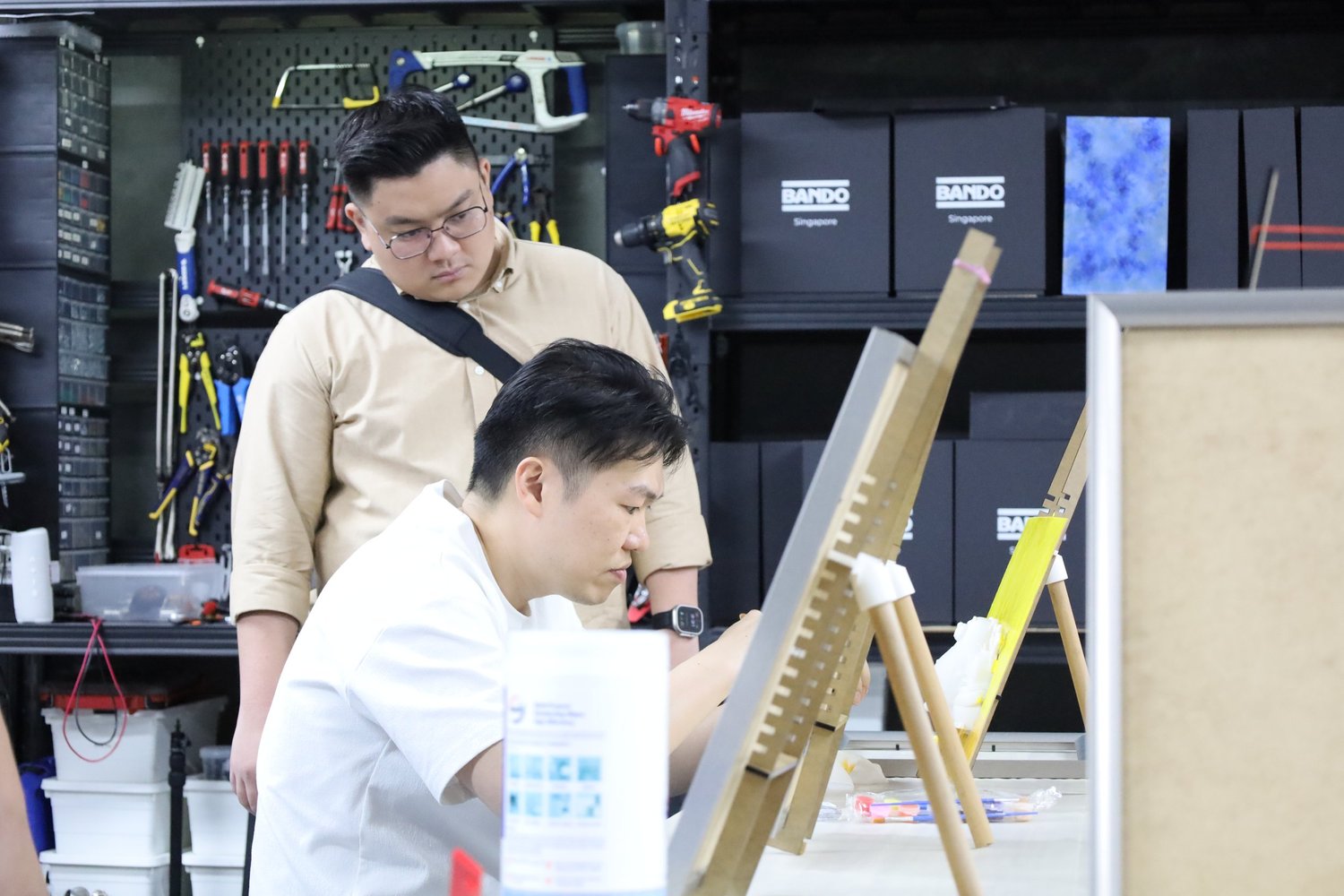Two guests painting at the workbench with the studio tool wall behind