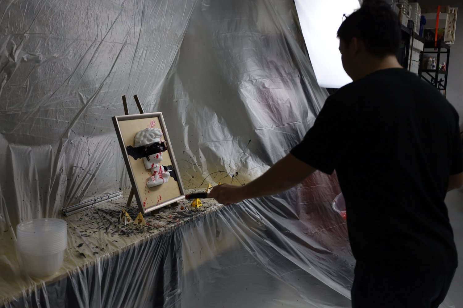 A guest splatter-painting a 3D piece under a protective sheet