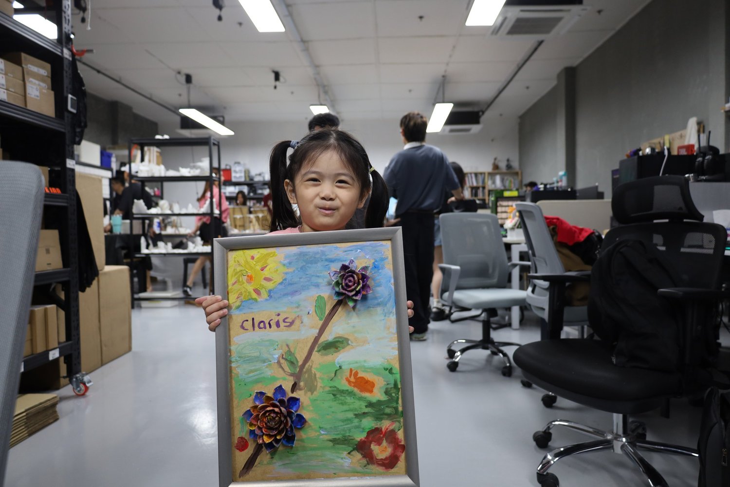A young girl holding up her painted flower canvas signed Claris