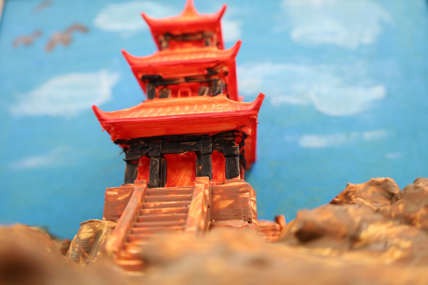 A finished red pagoda climbing a cliff against a blue painted sky