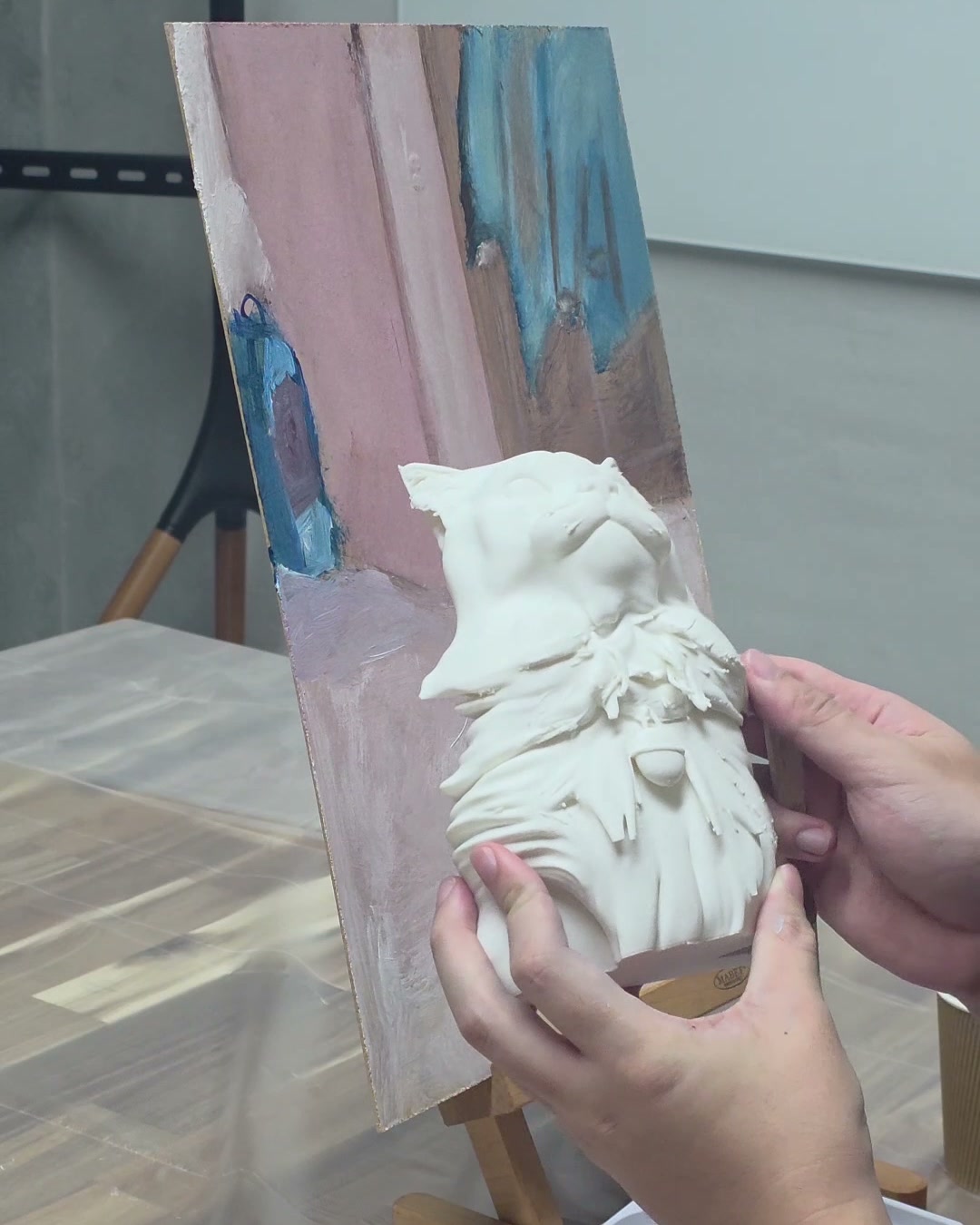 The unpainted white 3D print of the cat held against its canvas in the studio