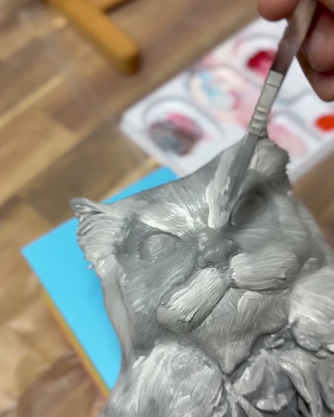 A brush painting the 3D-printed cat's face in soft greys